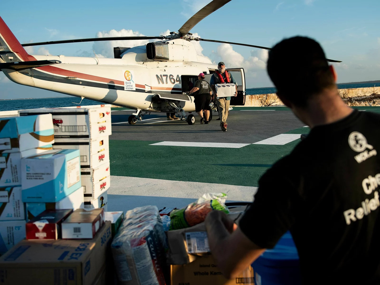 A helicopter full of crates of food being unloaded by workers